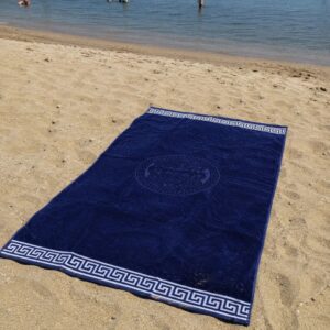 Telo mare blu navy in spugna 100% cotone con bordo greca bianco steso sulla sabbia vista dall'alto