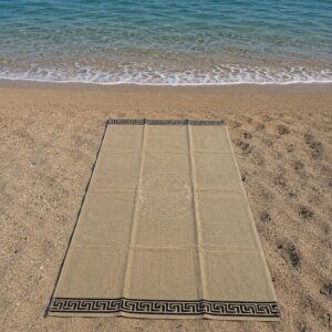 Telo mare spugna beige con bordo greca nero steso sulla sabbia della spiaggia vista dall'alto