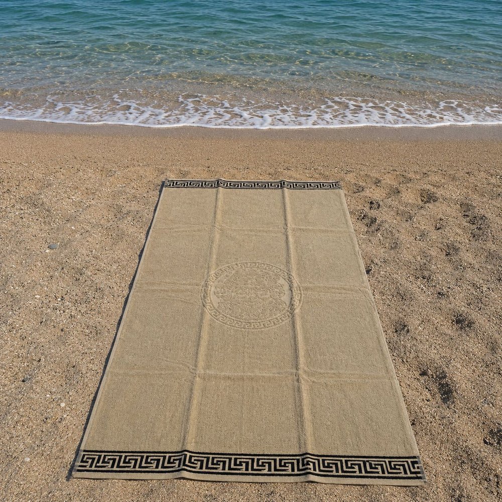 Telo mare spugna beige con bordo greca nero steso sulla sabbia della spiaggia vista dall'alto