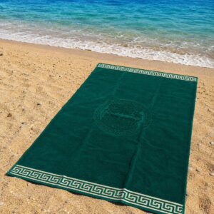 Telo mare verde smeraldo in spugna 100% cotone con bordo greca beige steso sulla sabbia fronte mare